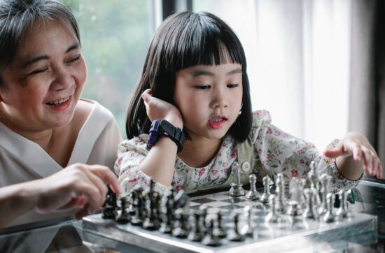 adorable ethnic child doing move while playing chess with grandmother